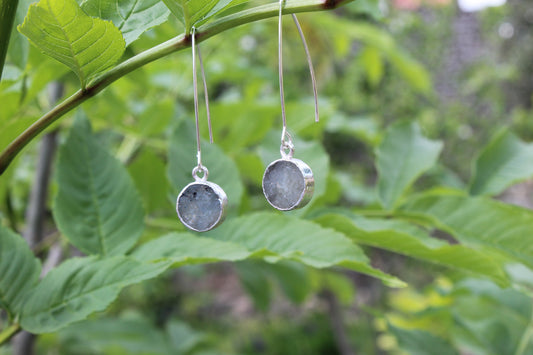 This image features a pair of elegant silver labradorite circle drop earrings. The earrings are crafted from sleek silver brass and showcase circular labradorite charms that beautifully capture and reflect light, creating a mesmerizing display of subtle flashes.