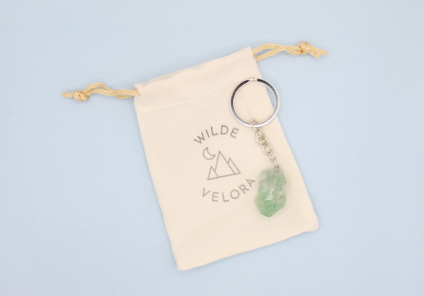 Keychain with green pendant on a beige pouch with 'Wilde Velora' branding against a light blue background