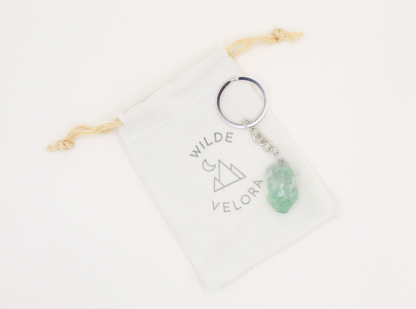 Keychain with green stone charm on a branded pouch against a white background