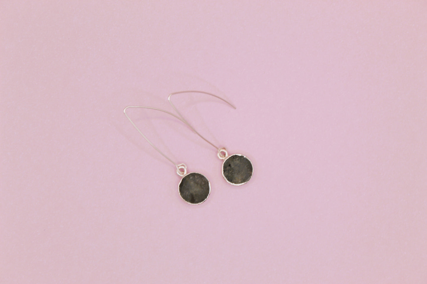 Pair of earrings with dark round stones on a pink background