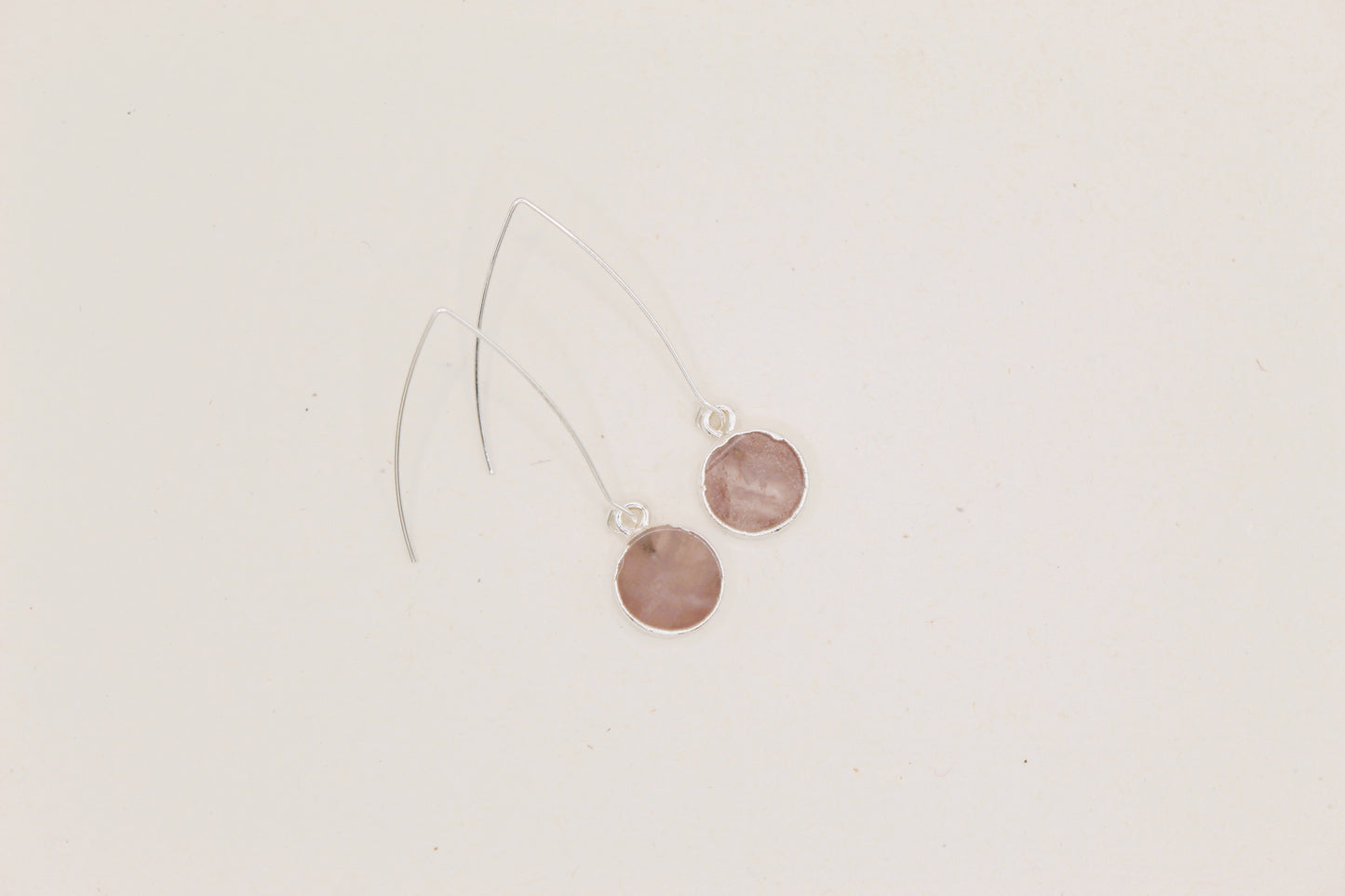 Pair of earrings with round pink stones on a light beige background
