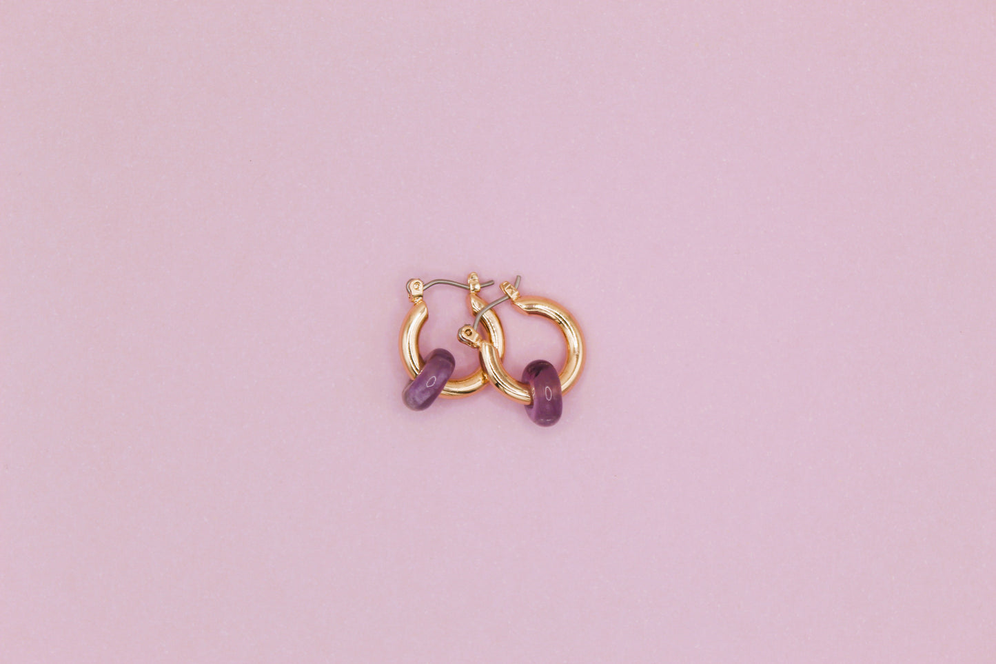 Gold hoop earrings with purple stones on a pink background