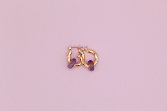 Gold hoop earrings with purple stones on a pink background