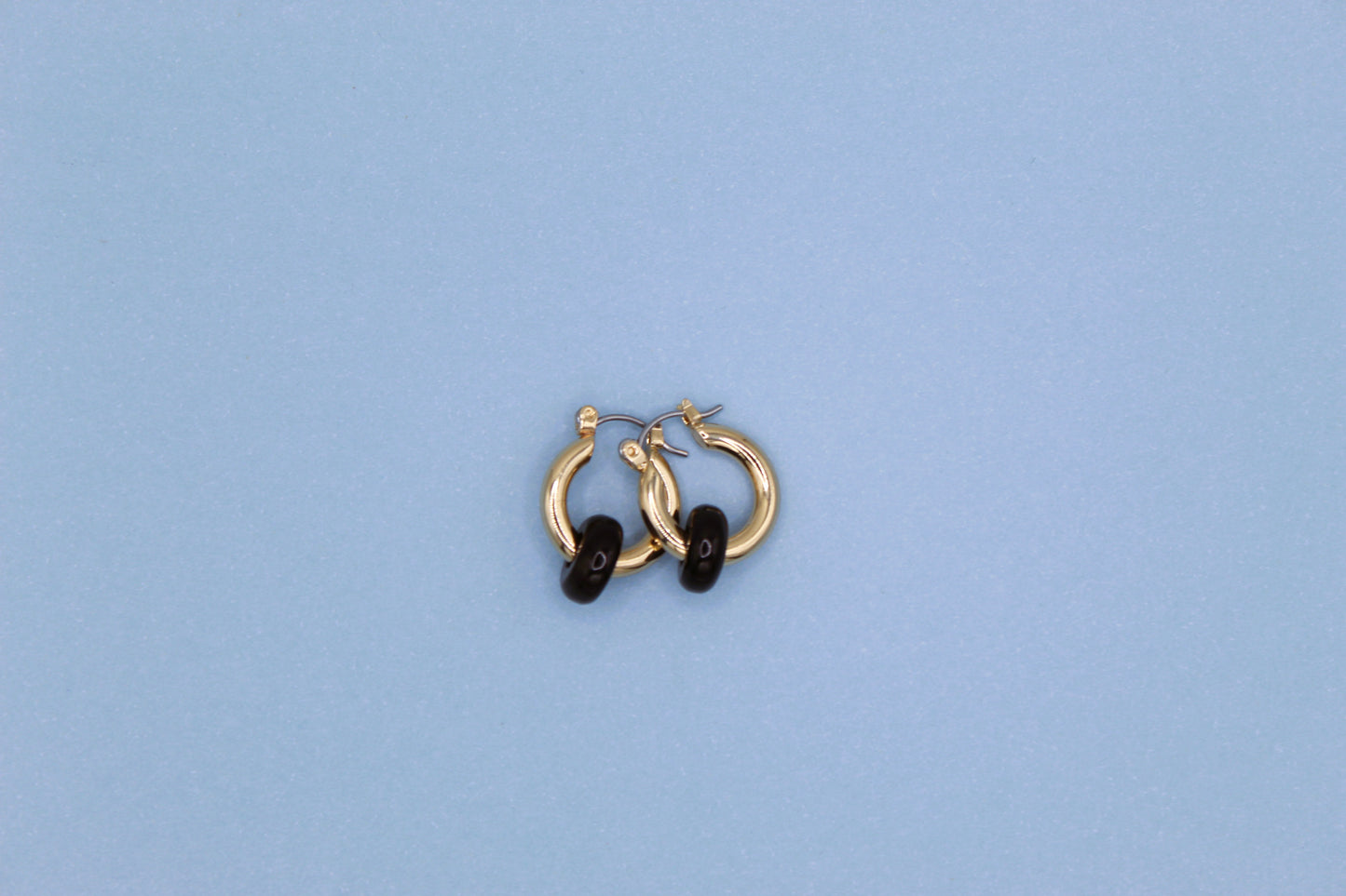 Gold hoop earrings with black stones on a light blue background