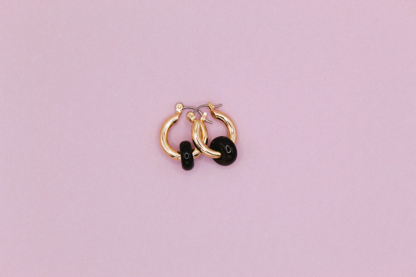 Pair of gold hoop earrings with black stones on a pink background