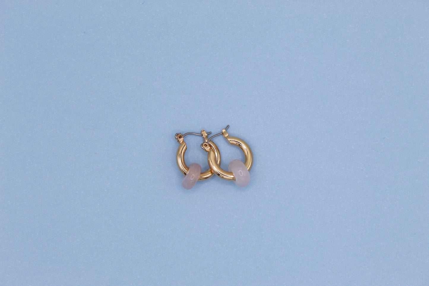 Gold hoop earrings with pink stones on a light blue background