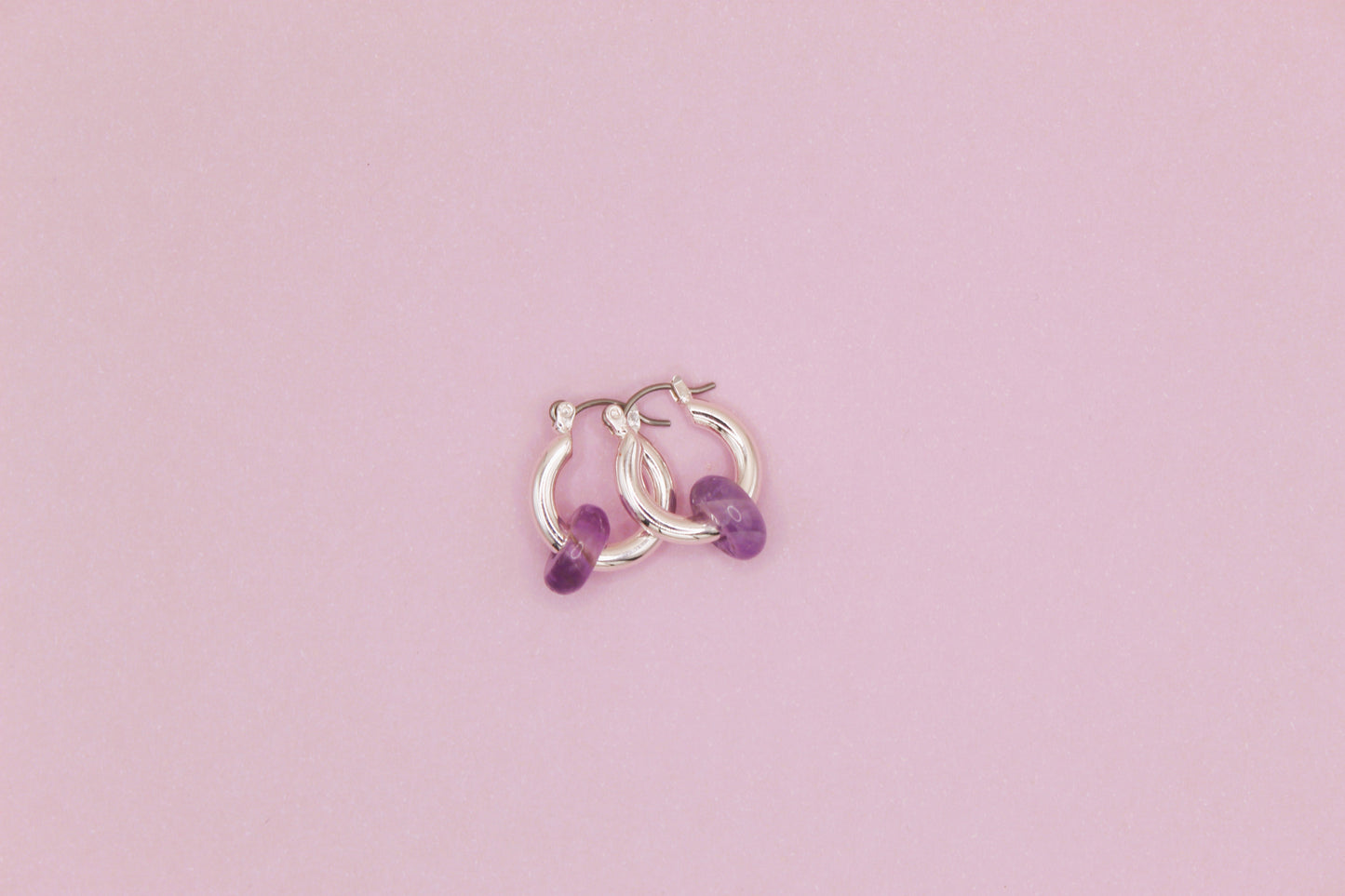 Silver hoop earrings with purple beads on a pink background