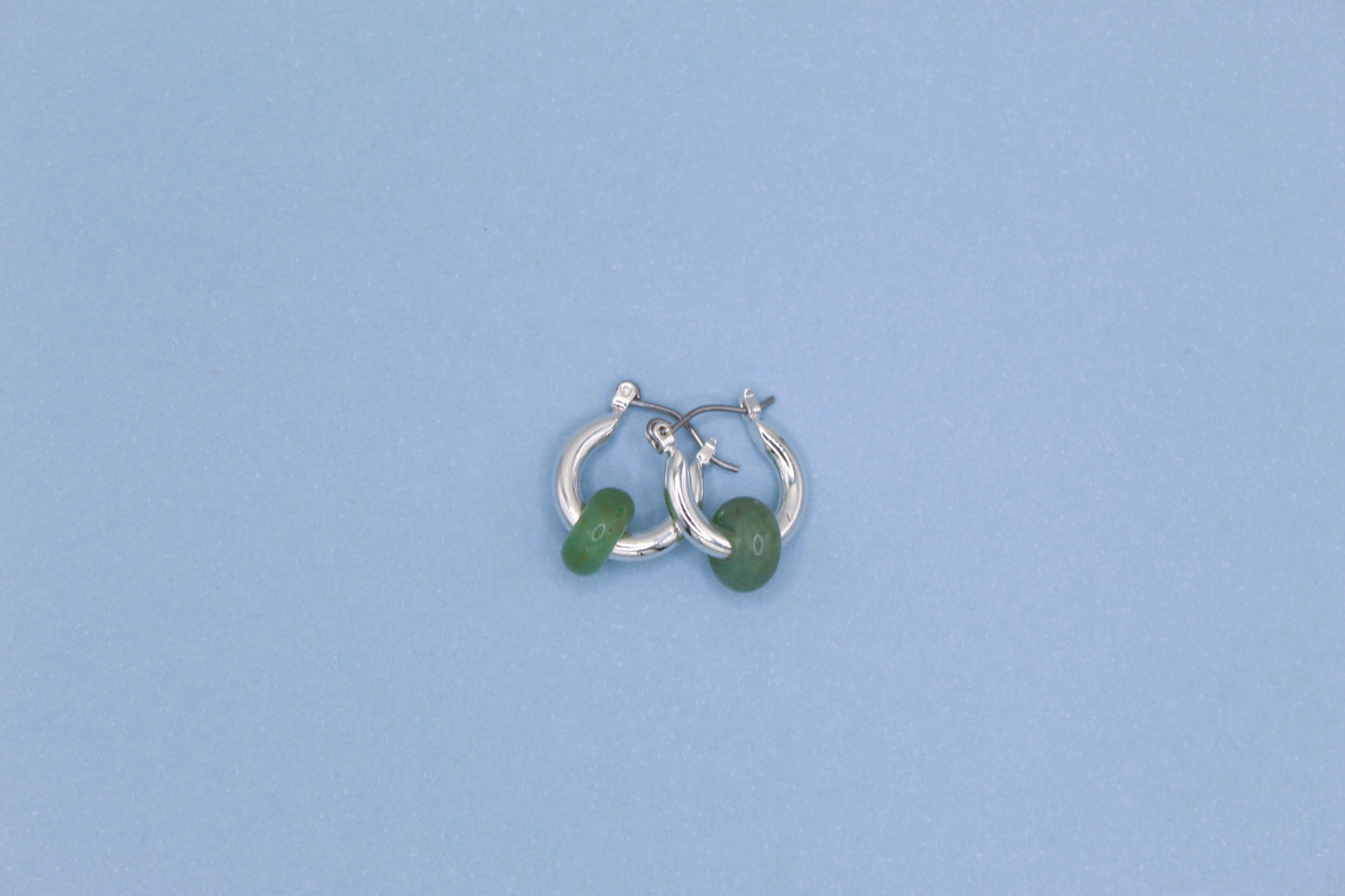Silver hoop earrings with green beads on a light blue background