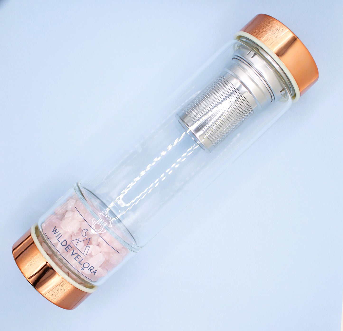 Clear glass bottle with rose gold cap and interior on a light blue background