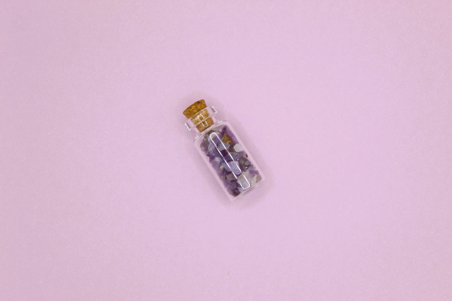 Small glass bottle with cork lid containing small stones on a pink background