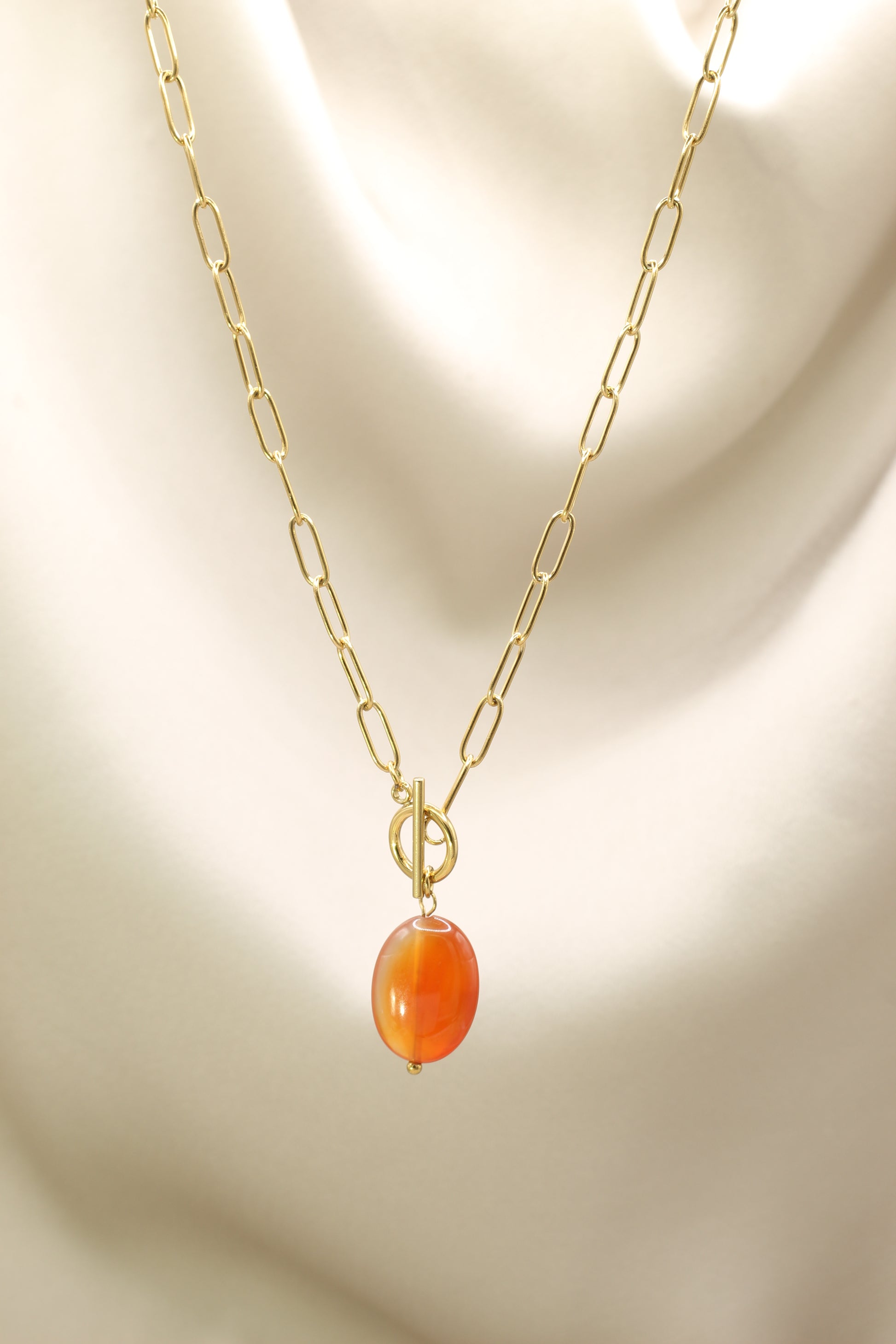 Gold necklace with an orange bead on a beige background