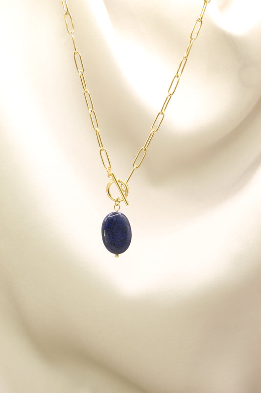 Gold chain necklace with a blue pendant on a beige background