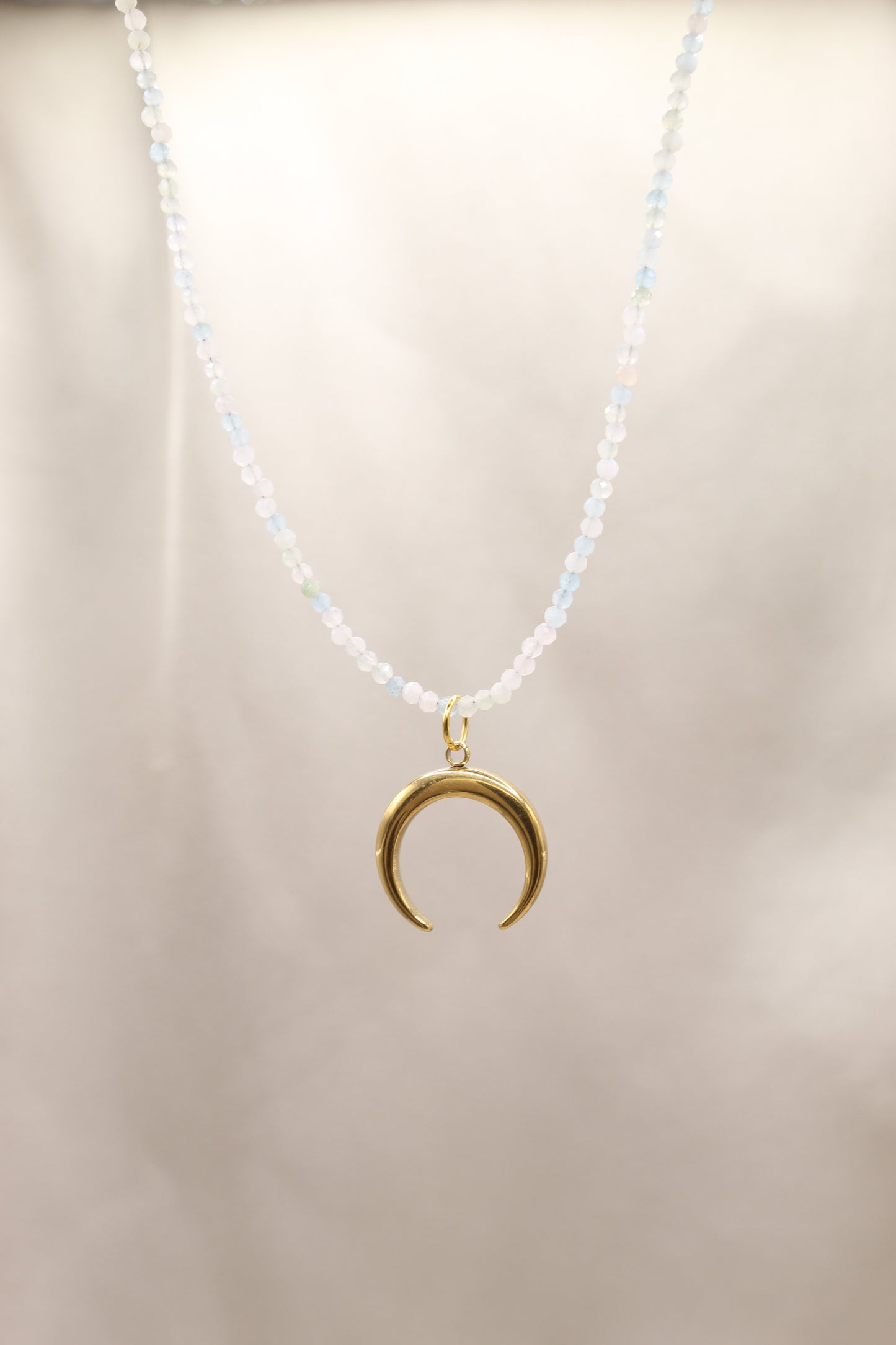Gold necklace with a crescent moon pendant on a beige background
