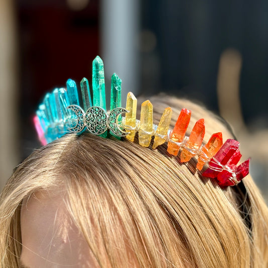 A close-up image of a person wearing a vibrant, multicolored crystal crown with a moon-and-branches design.