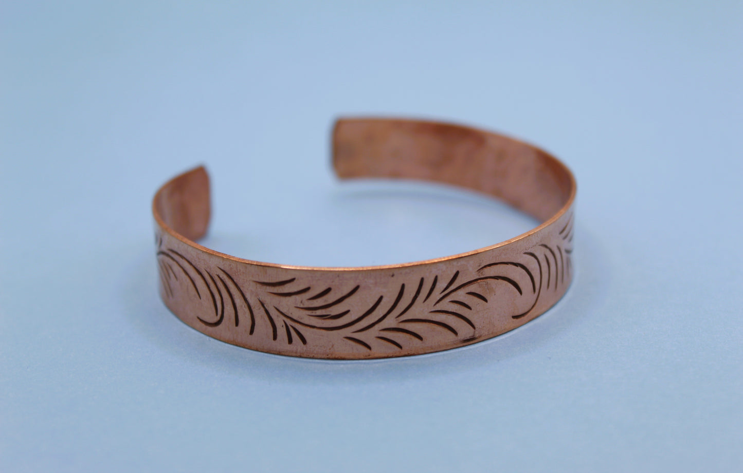 Copper bracelet with engraved design on a light blue background