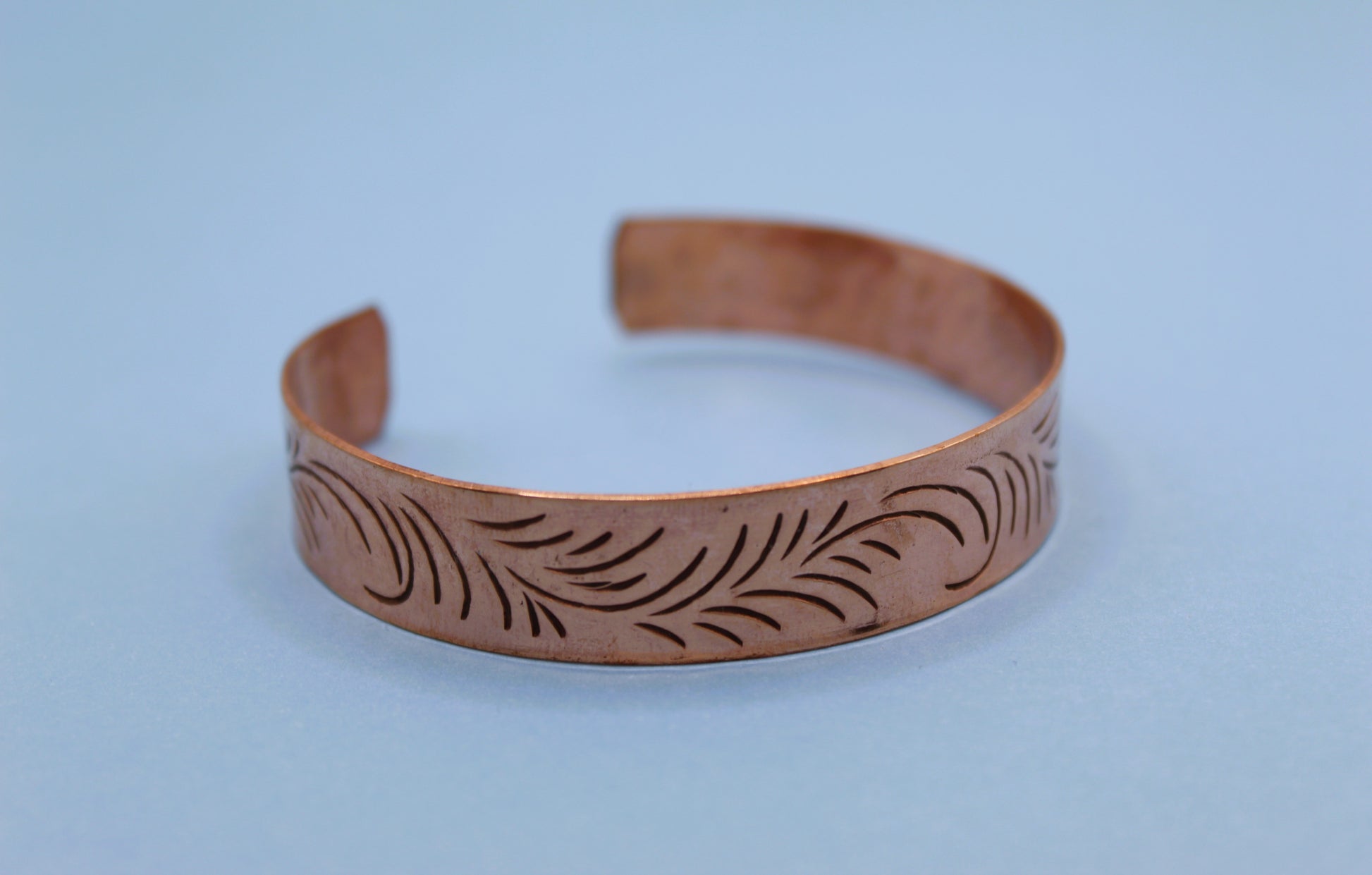 Copper bracelet with engraved design on a light blue background