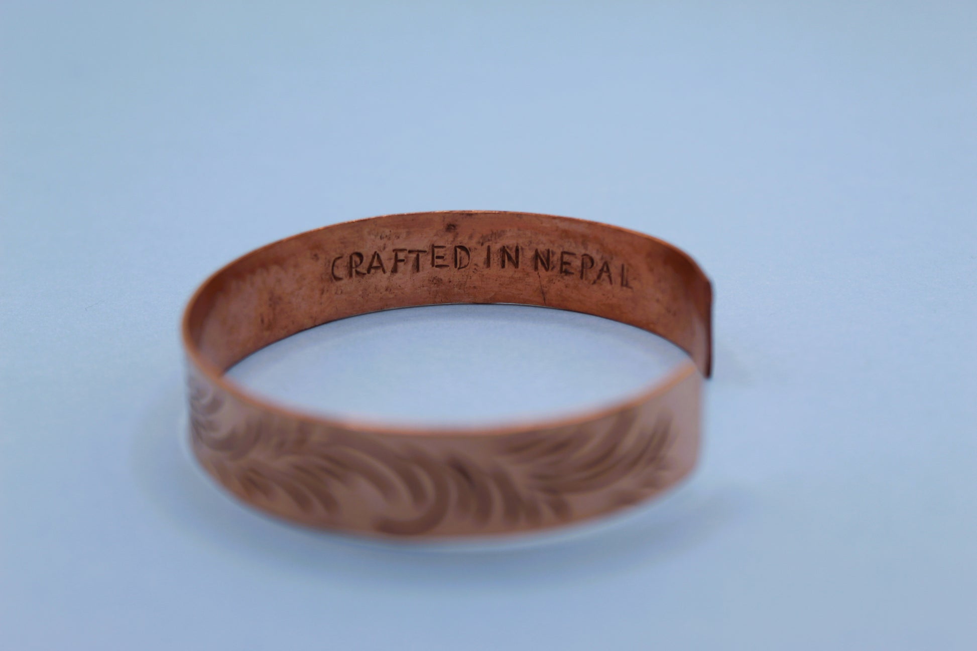 Brown leather wristband with 'Crafted in Nepal' engraving on a light blue background