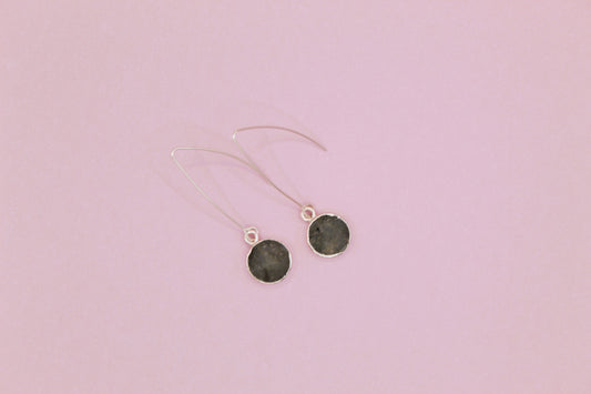 Pair of earrings with dark round stones on a pink background