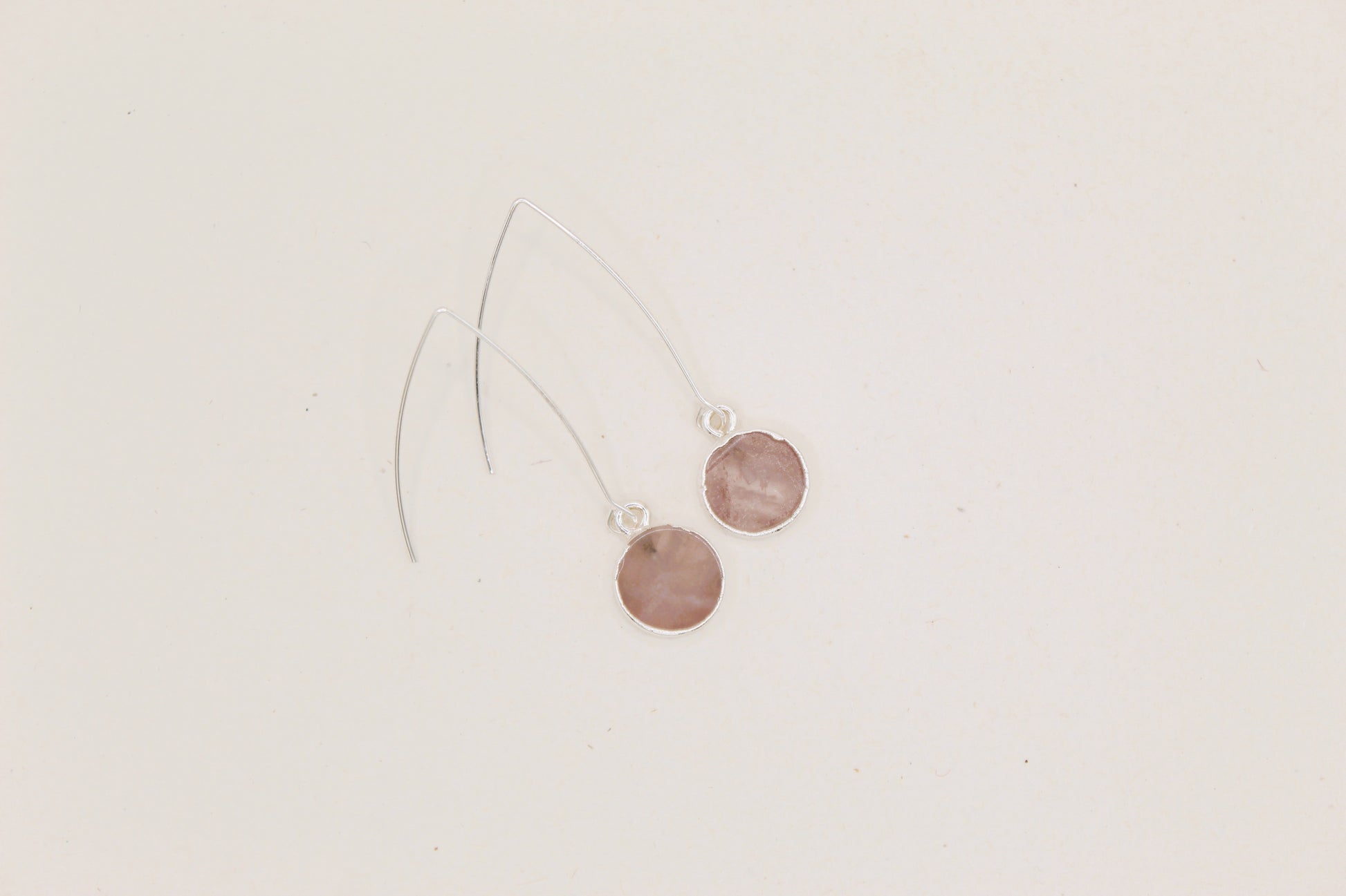 Pair of earrings with round pink stones on a light beige background
