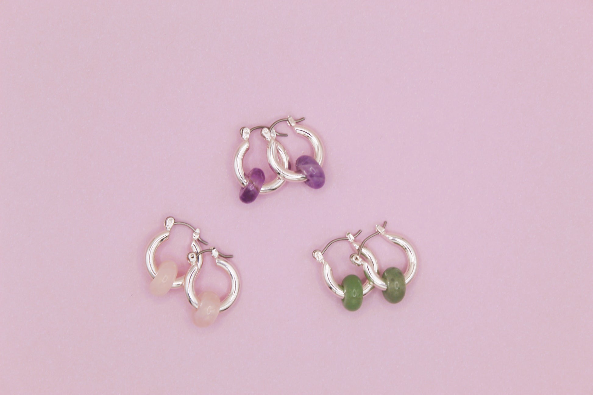  silver hoop earrings with gemstones on a pink background