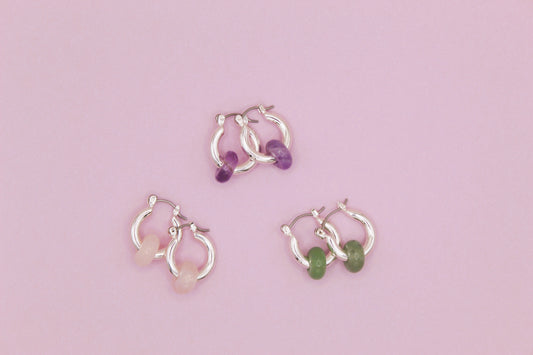  silver hoop earrings with gemstones on a pink background