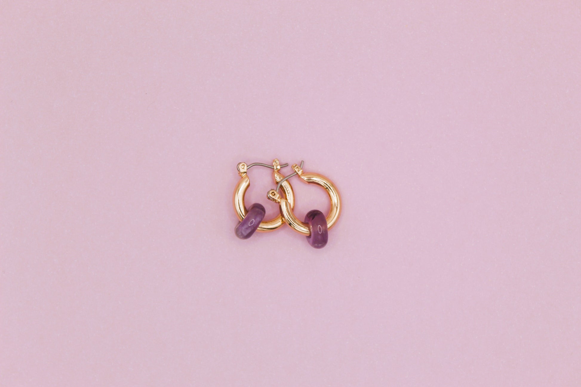 Gold hoop earrings with purple stones on a pink background