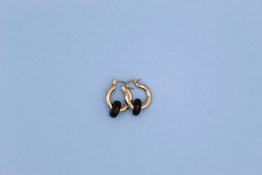 Gold hoop earrings with black stones on a light blue background