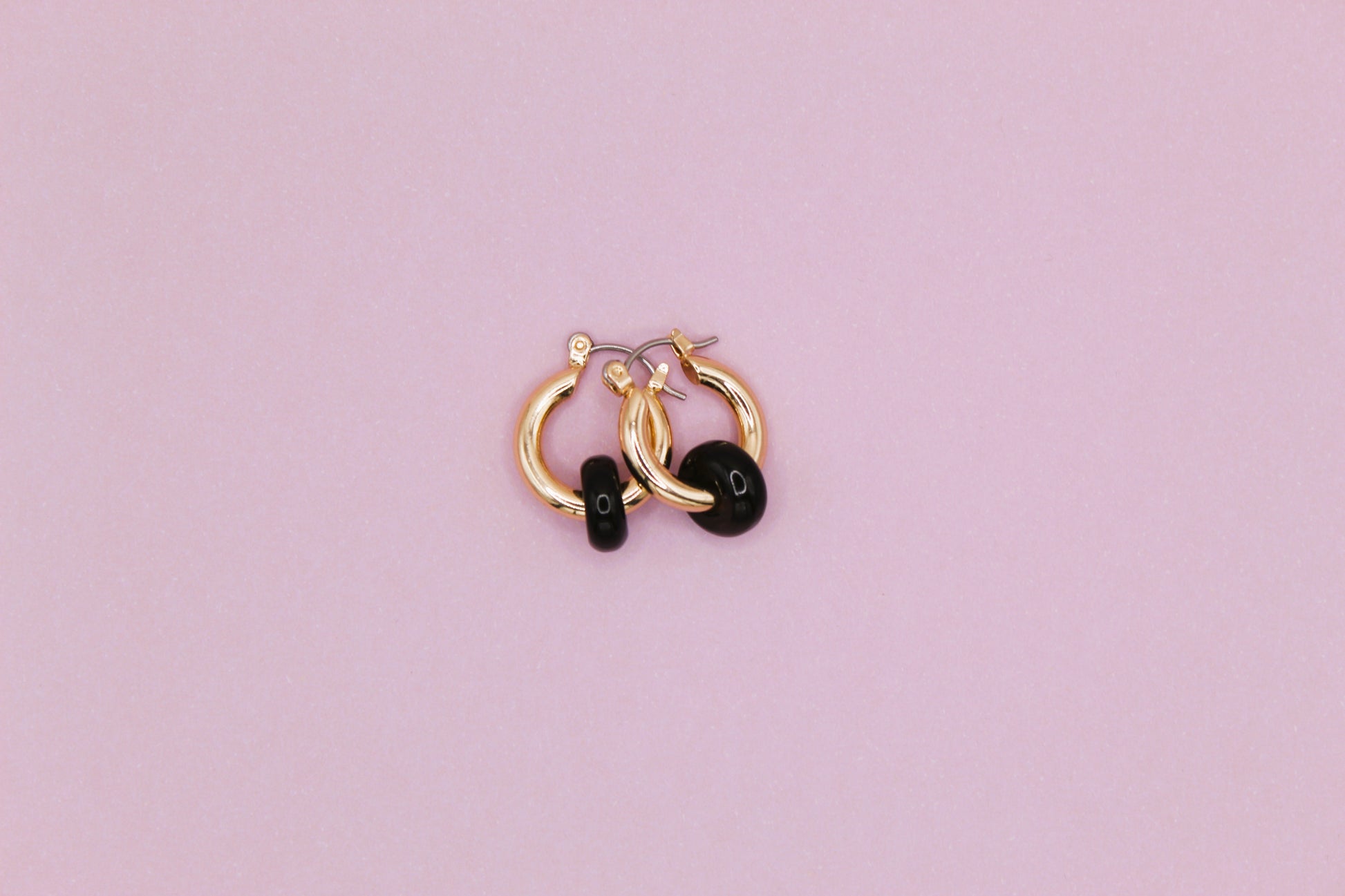 Pair of gold hoop earrings with black stones on a pink background