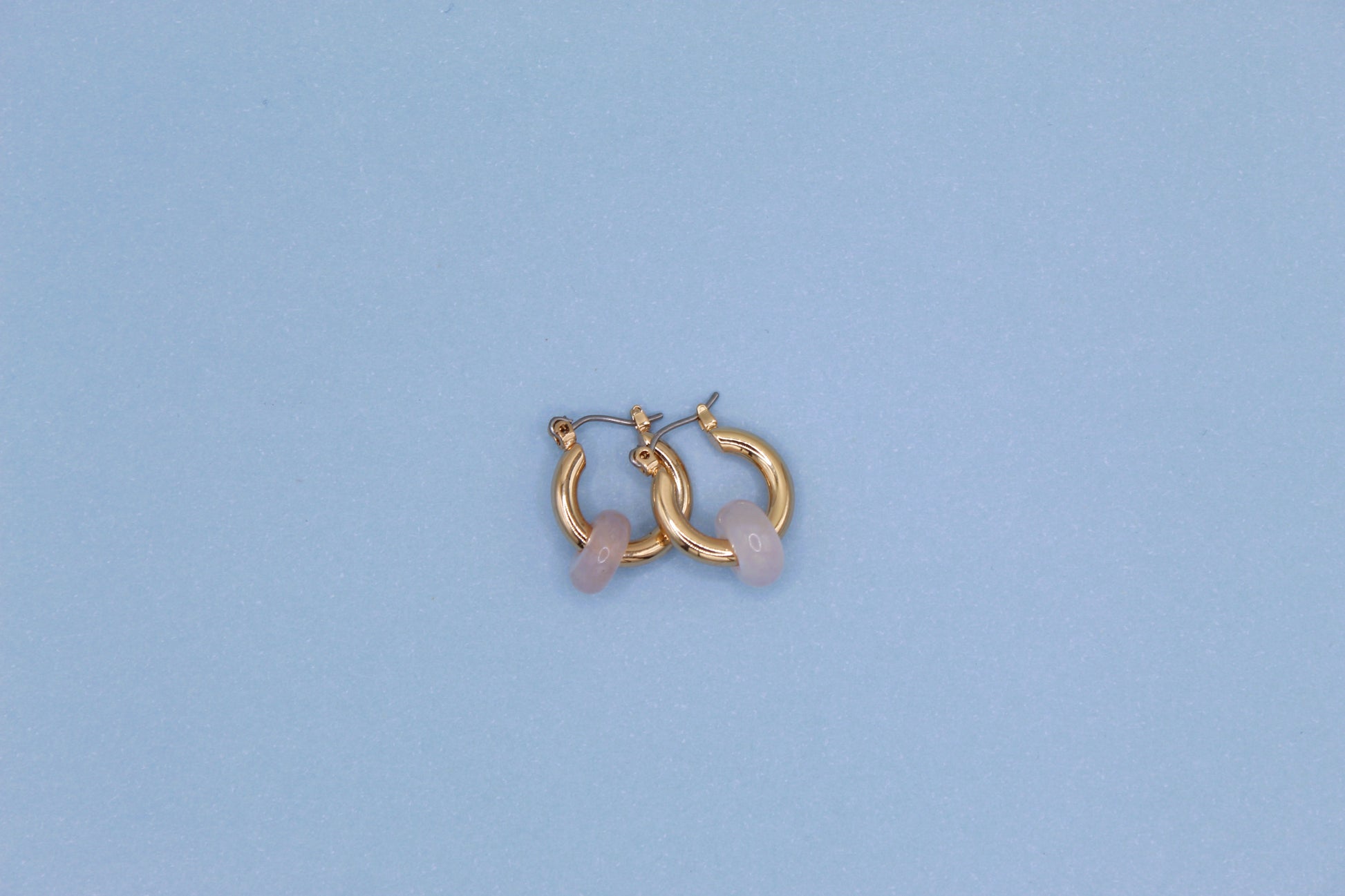 Gold hoop earrings with pink stones on a light blue background