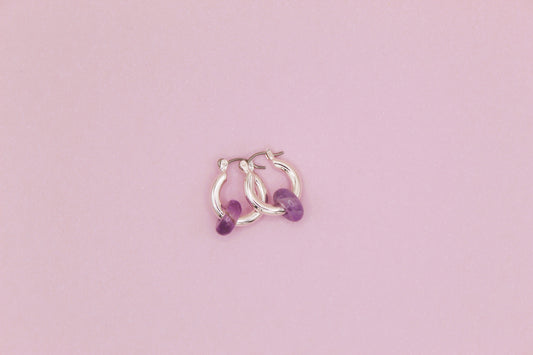 Silver hoop earrings with purple beads on a pink background