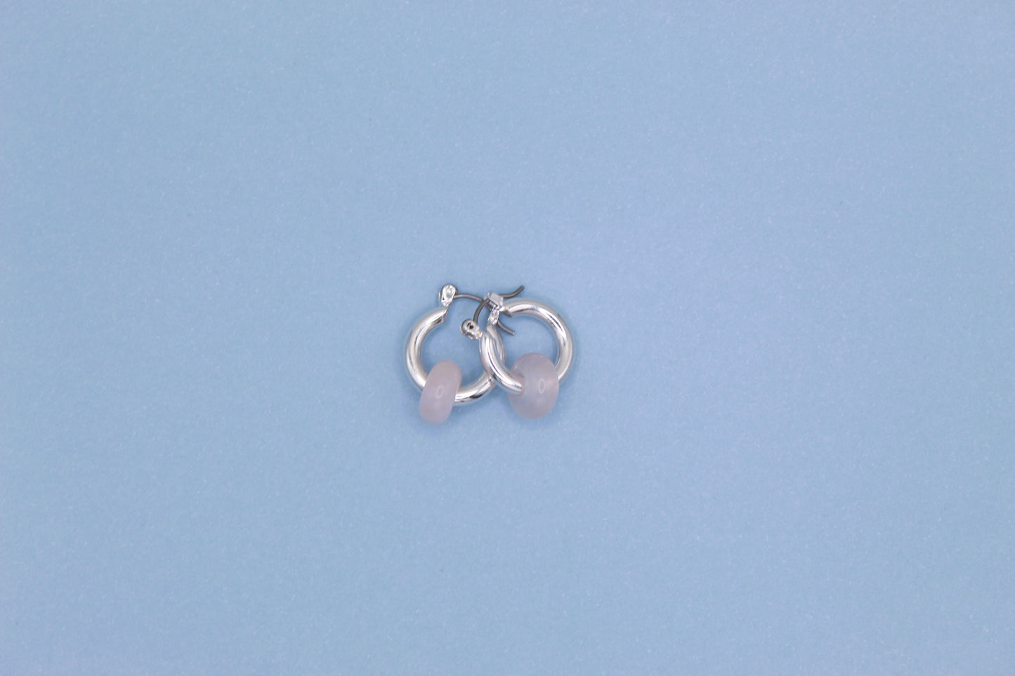 Silver hoop earrings with pink stones on a light blue background