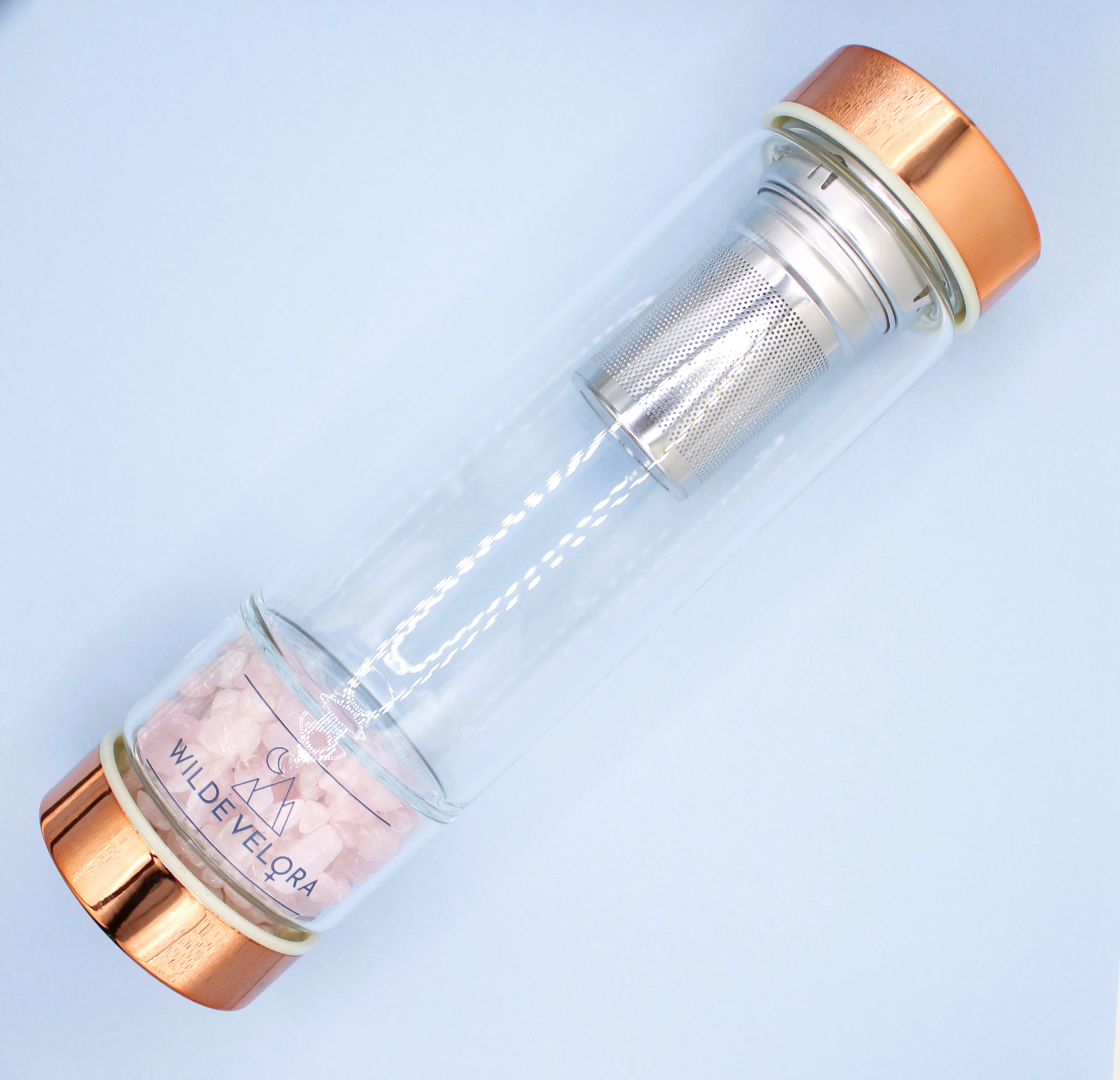 Clear glass bottle with rose gold cap and interior on a light blue background