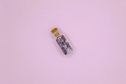Small glass bottle with cork lid containing small stones on a pink background